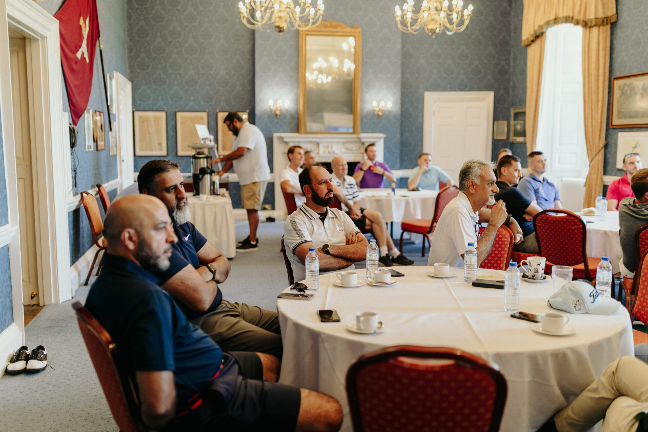 golf_pic10_guestsinarnhem_laying A group of men sitting by round tables in a blue room